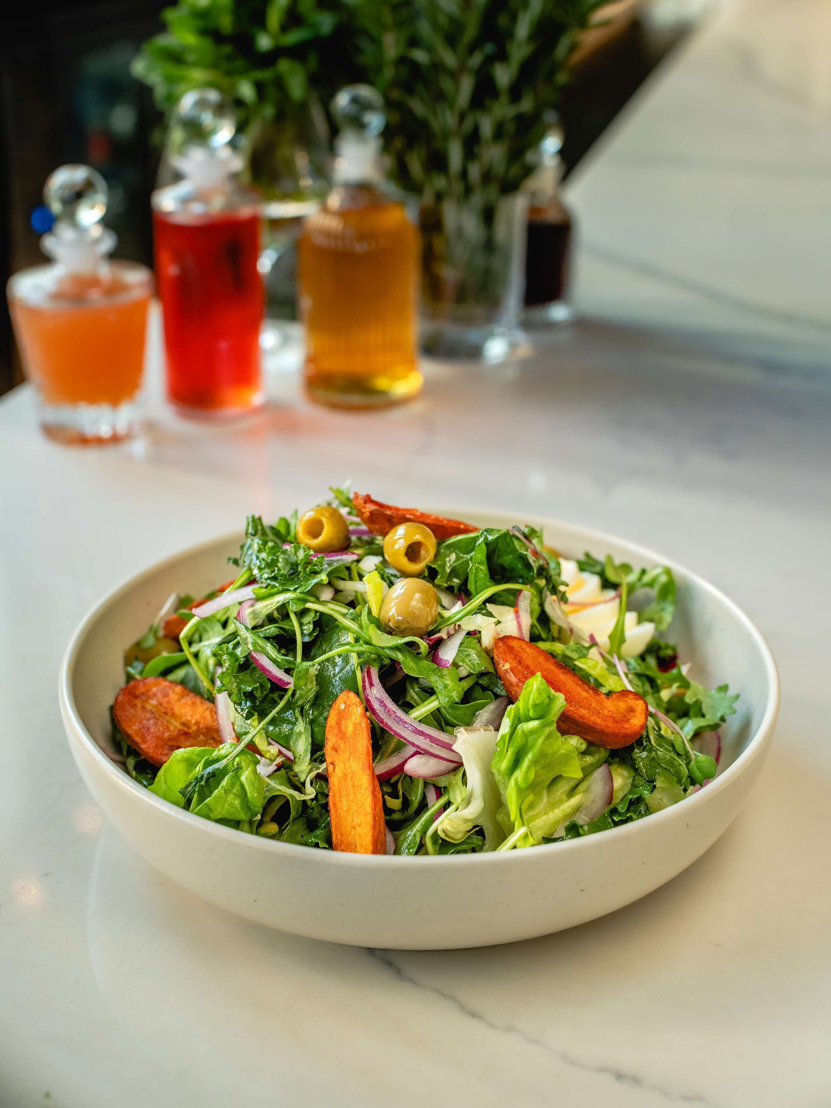 Un tazón de ensalada con diversos vegetales y un vaso de bebida roja al fondo.