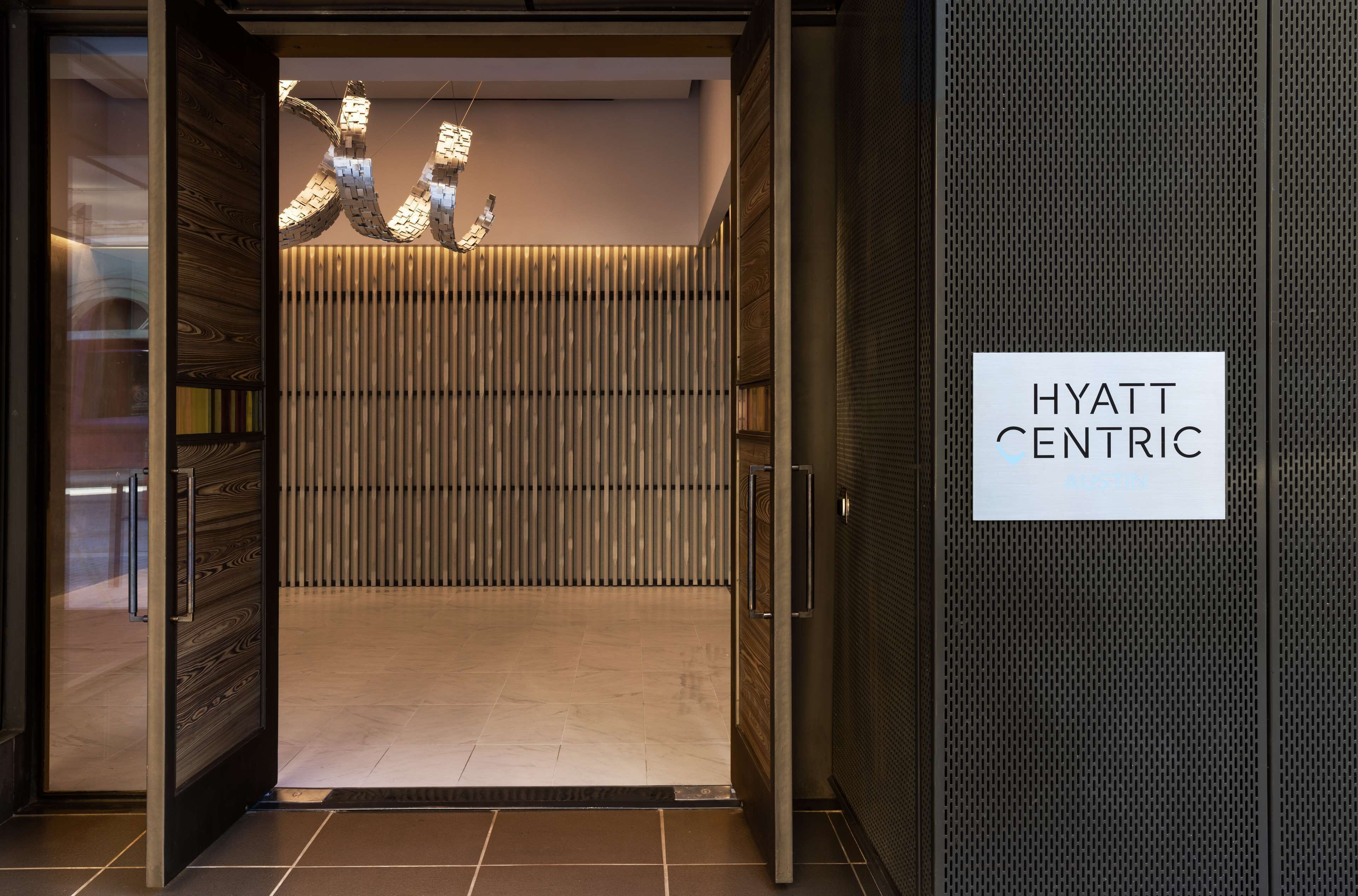 Der Eingang eines Hyatt Centric Hotels mit modernem Design, das eine Wand aus Holzpaneelen und ein Schild mit dem Hotelnamen zeigt.