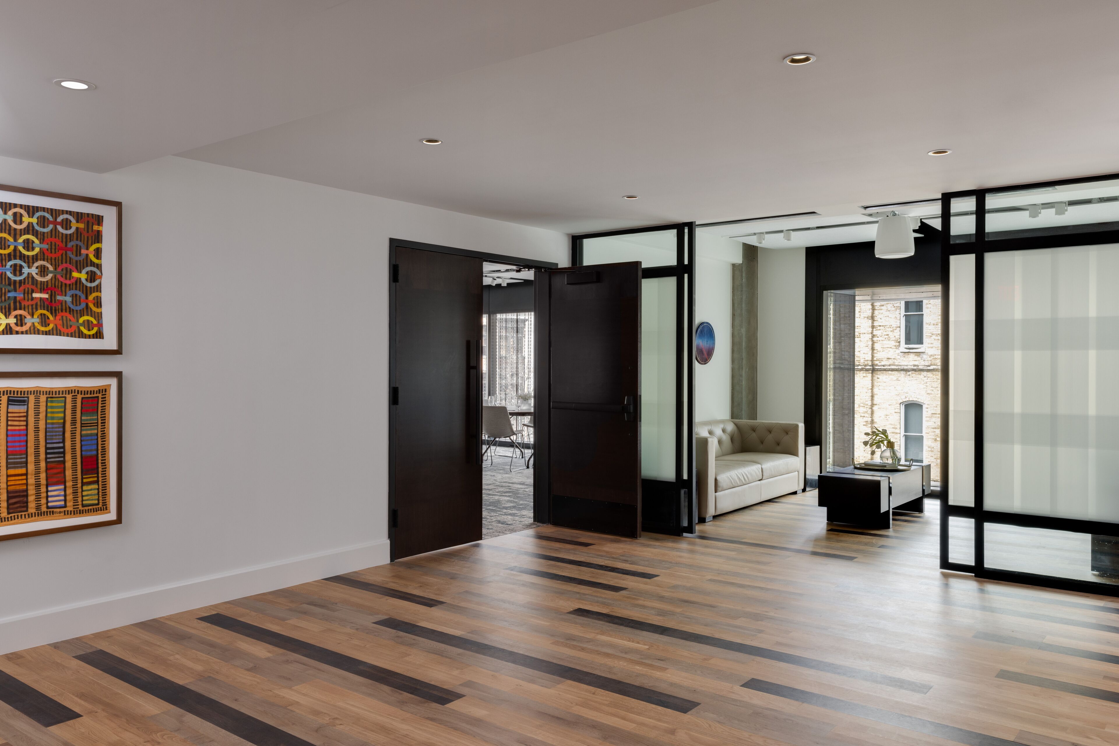 A modern interior with a wooden floor, a sofa, and a coffee table. There are two doors leading to other rooms.