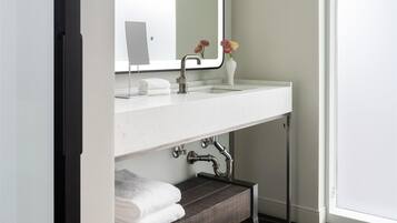 Um banheiro moderno com toucador branco, um espelho grande, um vaso com flores e um banco de madeira escura.