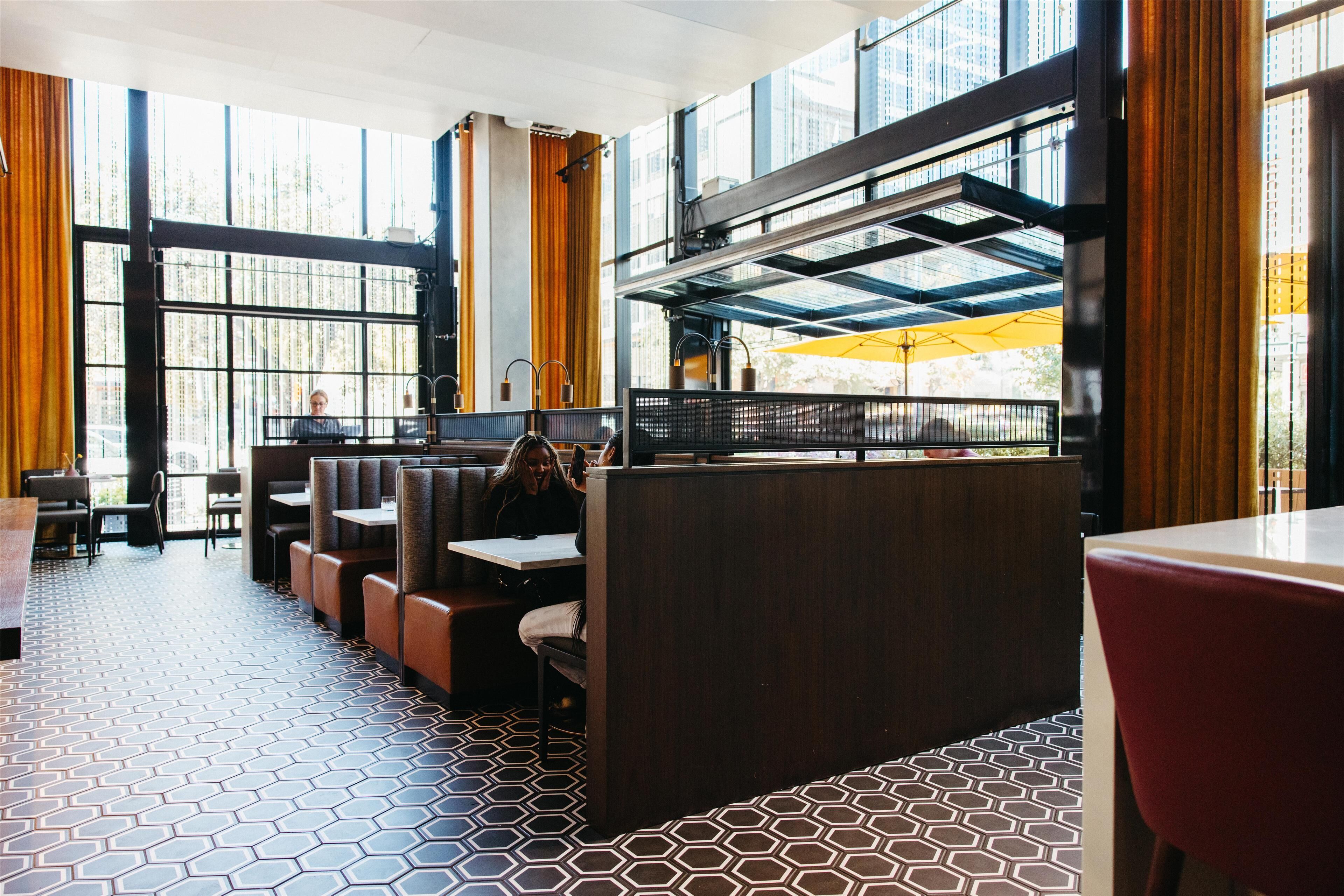A restaurant with high ceilings, large windows, and a geometric patterned floor.