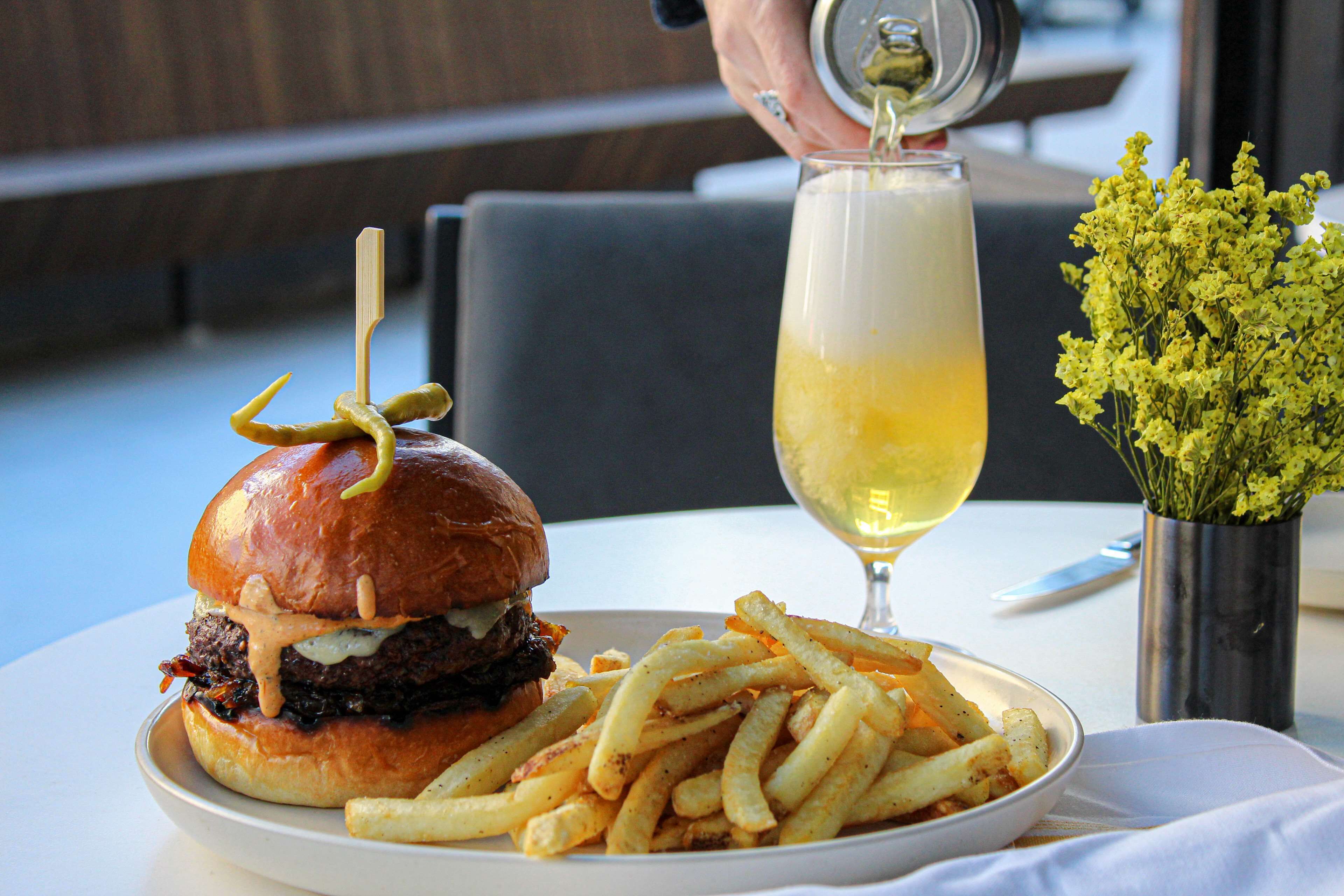 Et måltid bestående af en burger, pommes frites og et glas hvidvin på et bord.