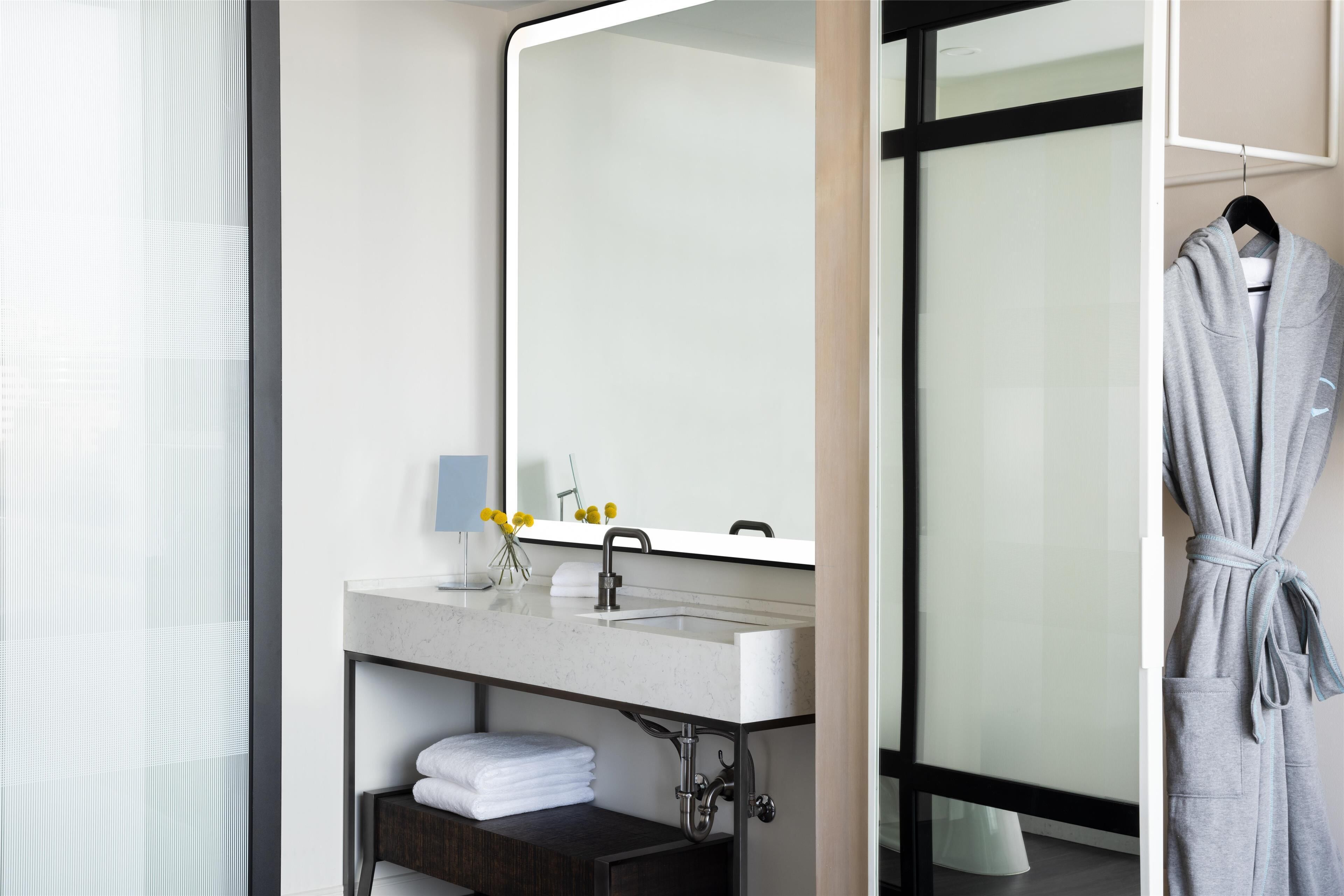 Un bagno moderno con un ampio specchio, un lavandino e un accappatoio appeso a un appendiabiti.