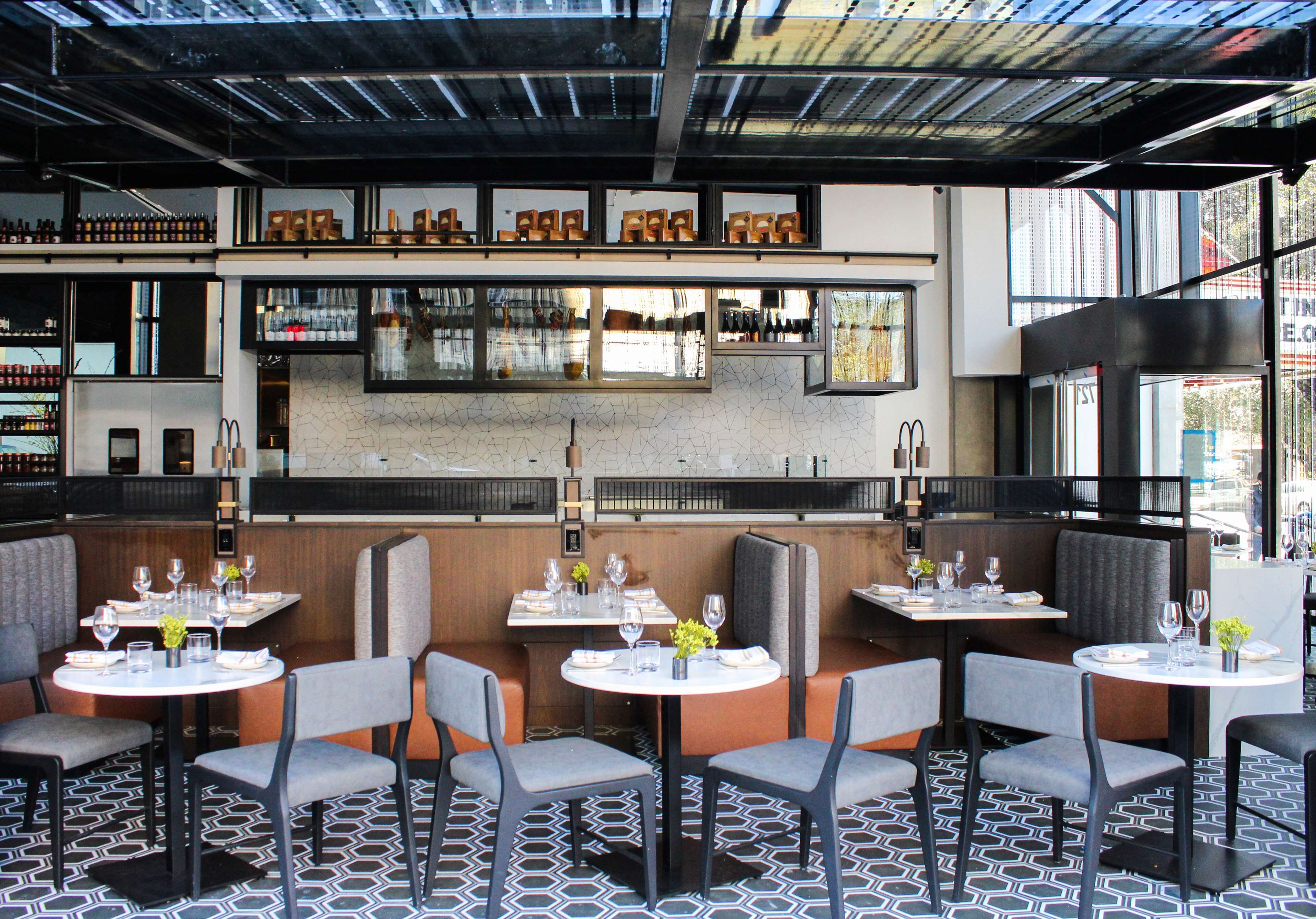 Interior de restaurante con varias mesas y cabinas, una zona de bar con botellas y un suelo con diseño.