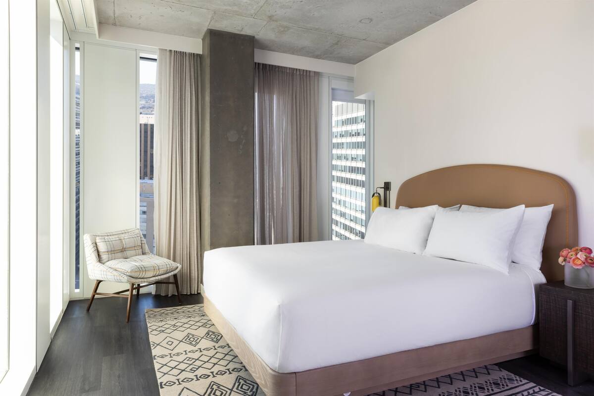 A hotel room with a large bed, a chair, a nightstand, and a view of the city.