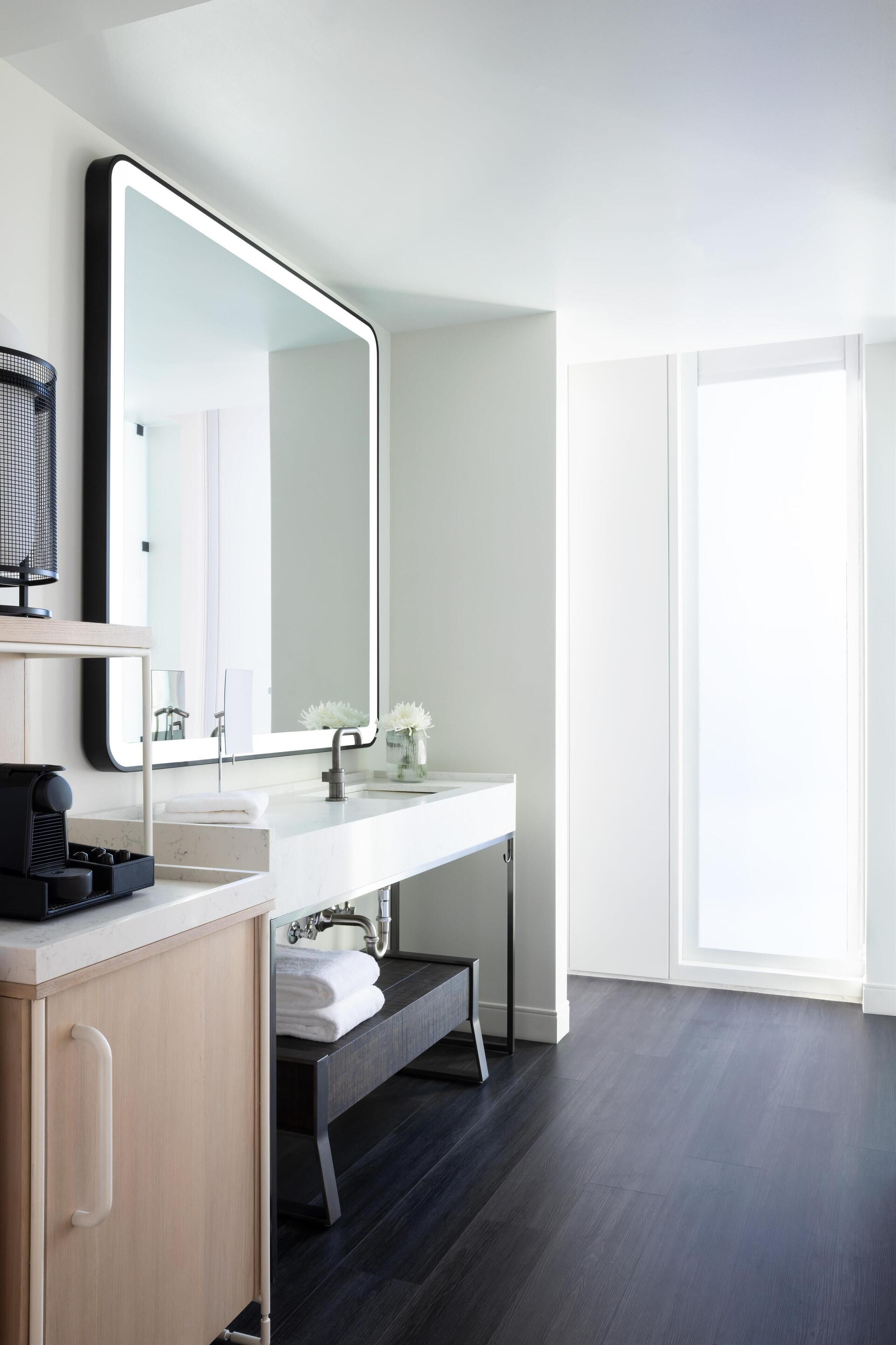 Een moderne badkamer met een grote spiegel, een witte wastafel en een vloer van donker hout.