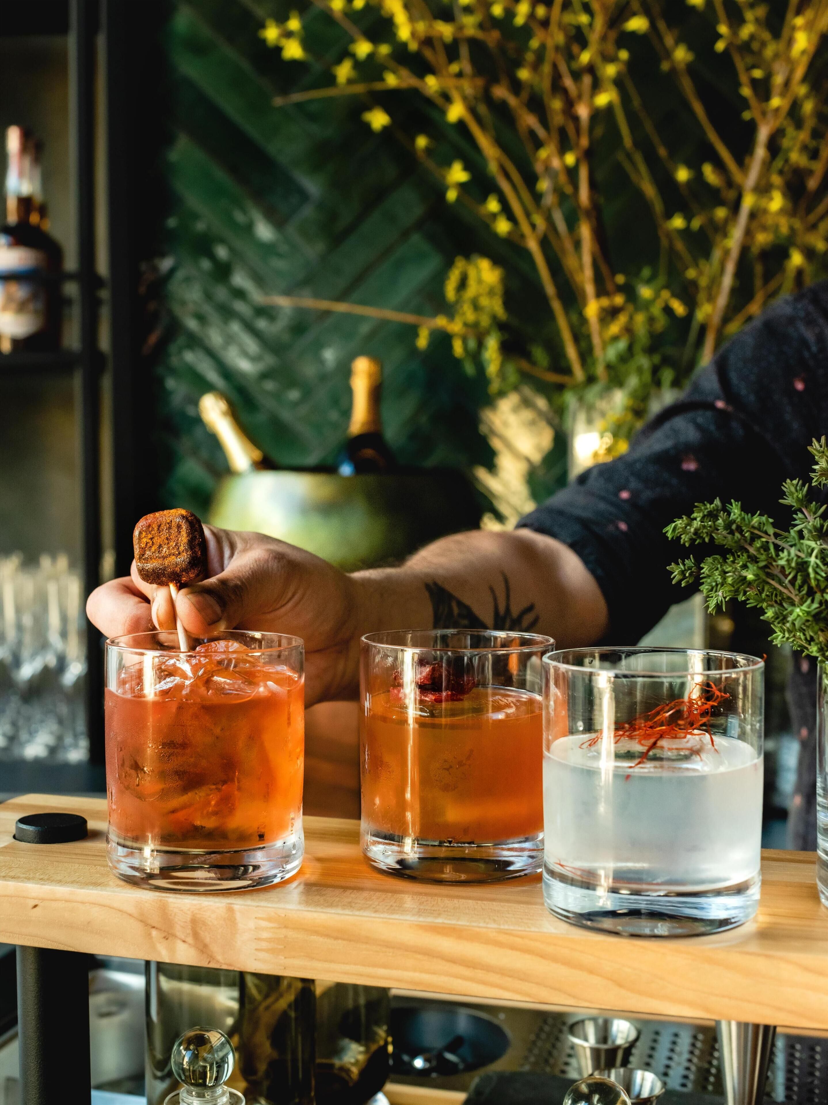 Un bar avec trois verres contenant une boisson rougeâtre, une bouteille de champagne et une plante décorative.