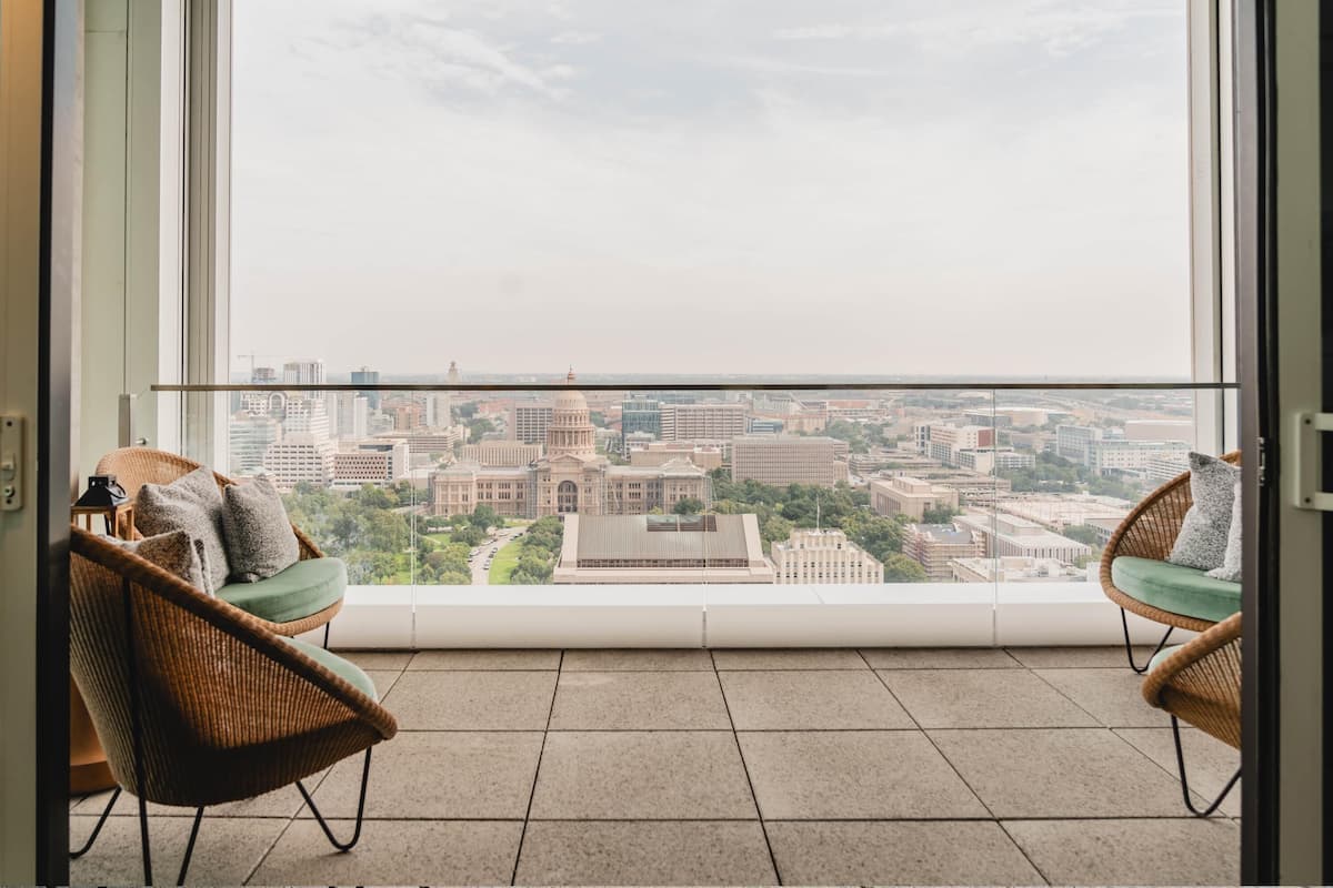 A balcony with two wicker chairs and a view of a cityscape.