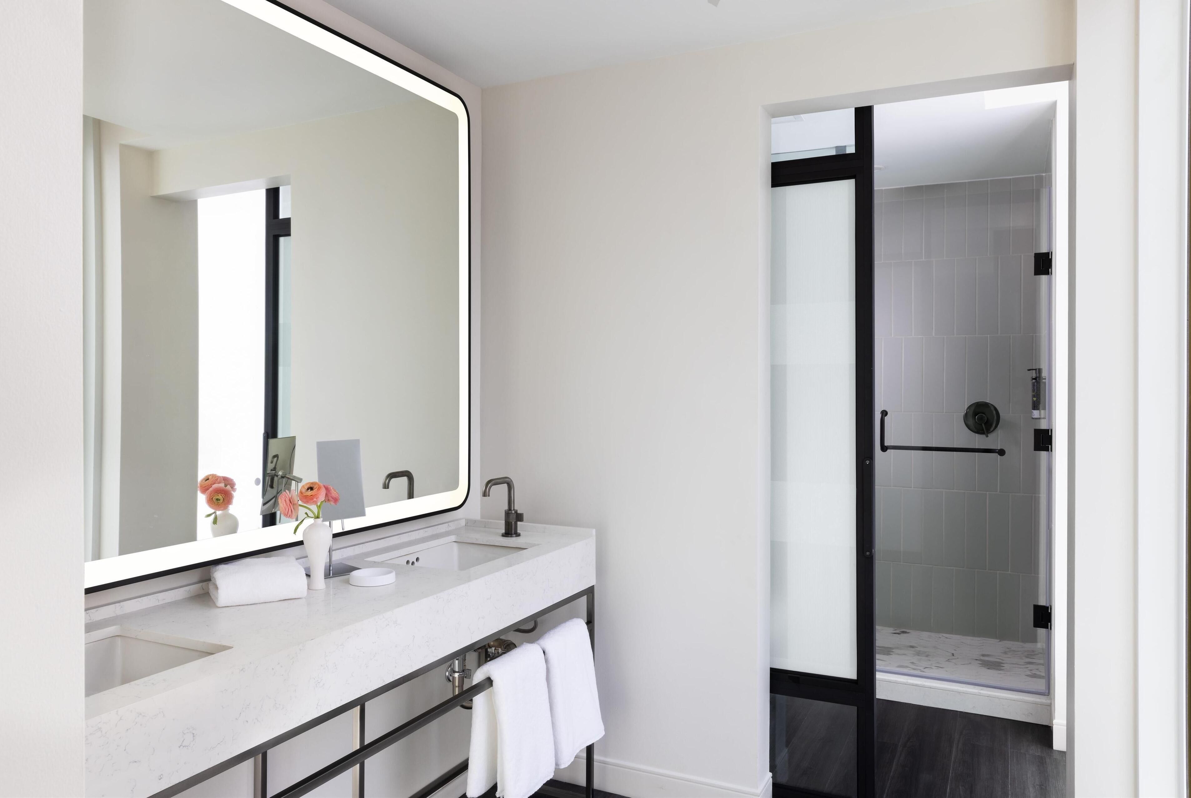 A modern bathroom with a large mirror, white marble sink, and a glass-enclosed shower.