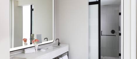 A modern bathroom with a large mirror, white marble sink, and a glass-enclosed shower.