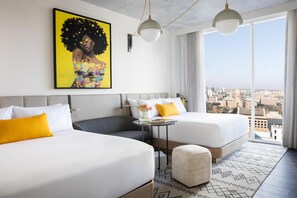 A hotel room with two beds, a small table with a vase of flowers, and a view of the city through large windows. - Hyatt Centric Congress Ave Austin (Austin)