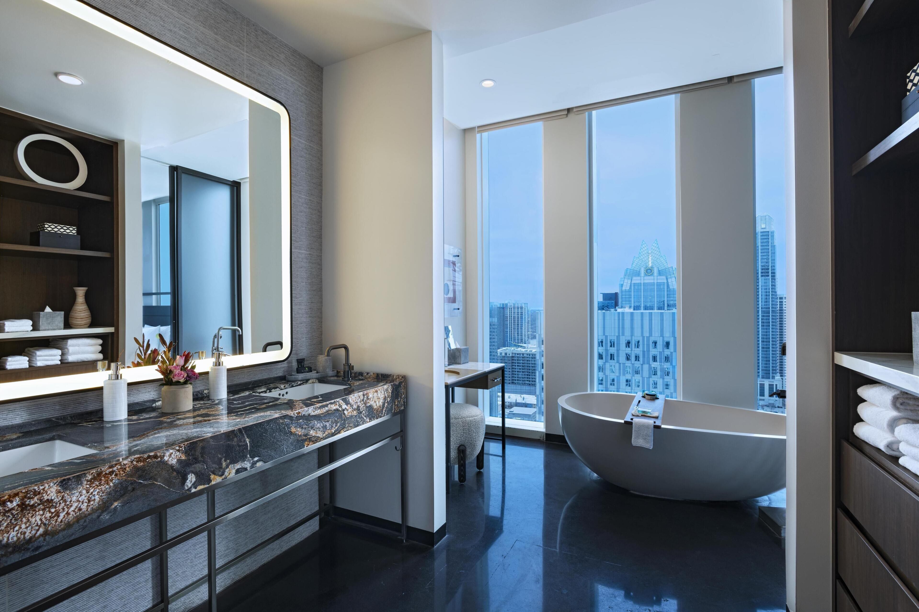 Un baño moderno con un espejo grande, una bañera y vistas a la ciudad.