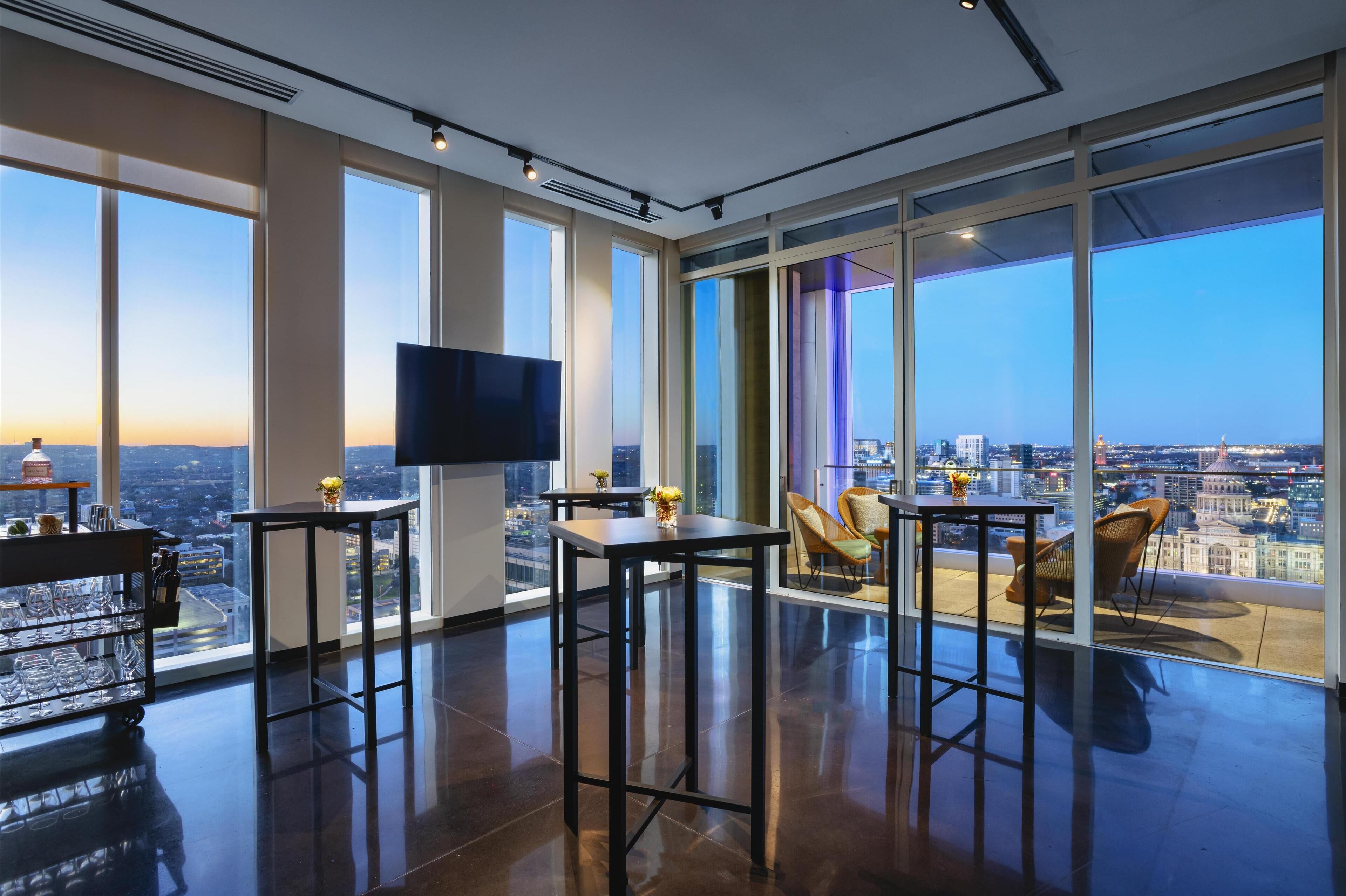 A modern interior with large windows, a flat-screen TV, and a dining area with chairs and tables.