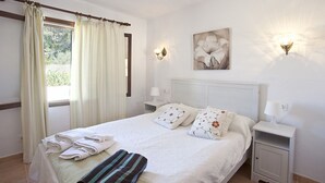 A neatly made bed with pillows, a bedside table with a lamp, and a window with curtains. - Ideal for families with pool, Can Seguinot (Pollensa / Pollença)