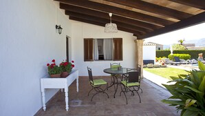 A patio with a round table and chairs, a white bench with potted red flowers, and a hanging light fixture. - Ideal for families with pool, Can Seguinot (Pollensa / Pollença)