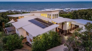Une maison moderne dotée d’un grand toit, de panneaux solaires et offrant une vue sur l’océan.