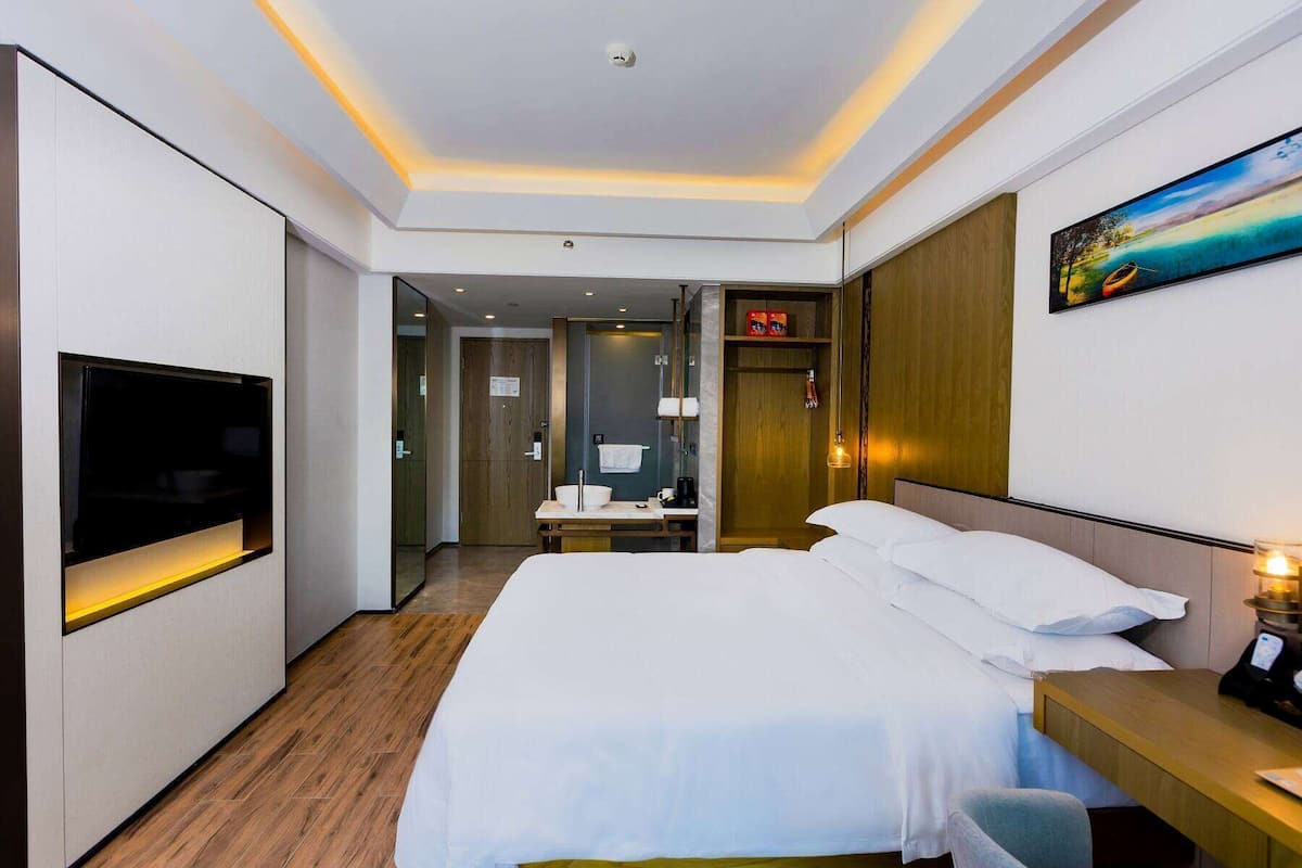 A modern hotel room with a large bed, a TV mounted on the wall, a wooden desk, and a painting on the wall.