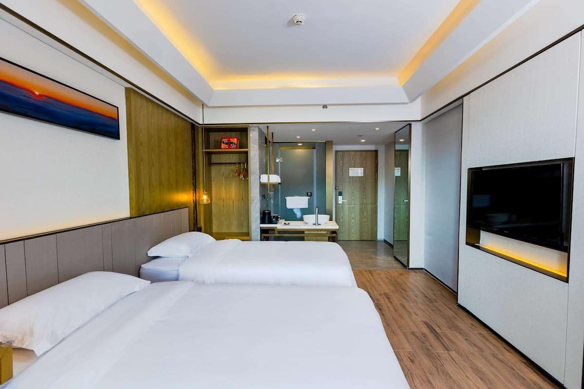 A hotel room with a large bed, a TV, a desk, and a bathroom visible through an open door.