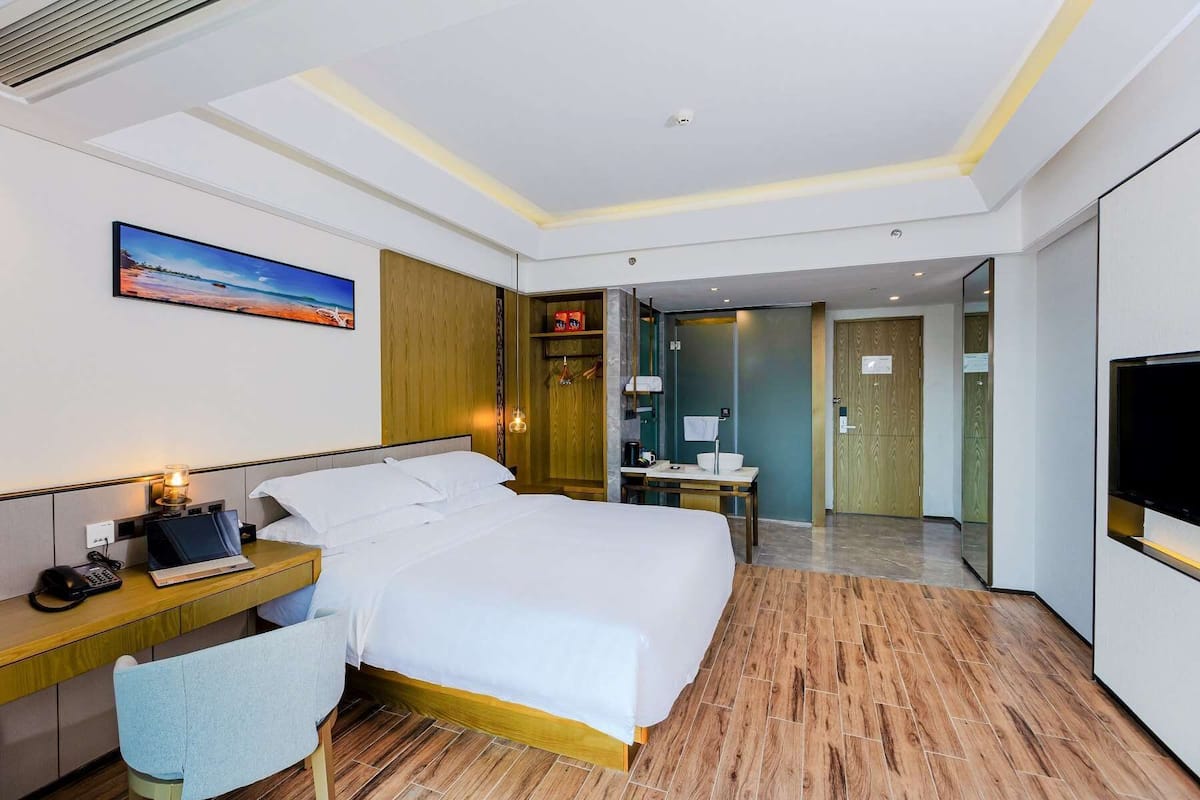 A hotel room with a bed, bedside table, lamp, and a TV.