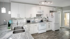 A modern kitchen with white cabinets, a stainless steel sink, a microwave, a stove, and a refrigerator. - Coastal Getaway - Steps from the Beach! (Cape Canaveral)