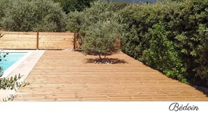 Una terraza de madera con piscina, rodeada de vegetación y una montaña al fondo.