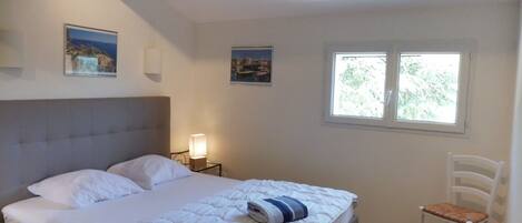A bedroom with a bed, a bedside table with a lamp, a chair, and two windows.