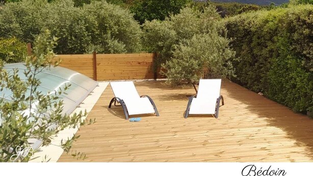 Una terraza de madera con dos sillones de descanso y una piscina, rodeada de follaje y montañas al fondo.