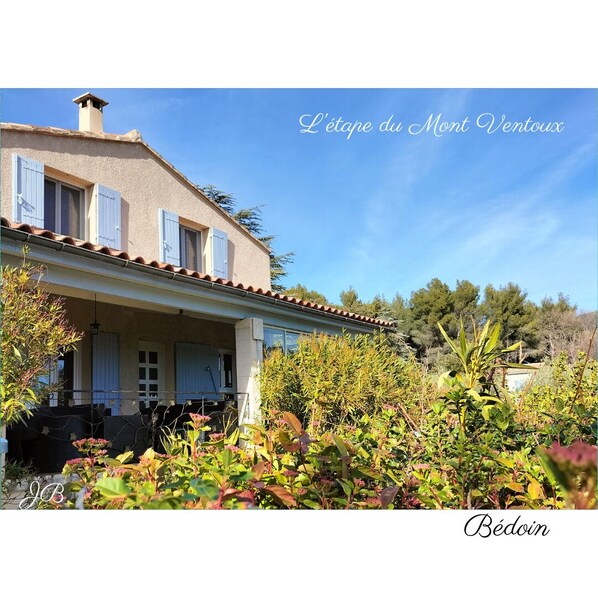 A traditional Mediterranean-style house with a tiled roof, a balcony, and a garden with various plants.