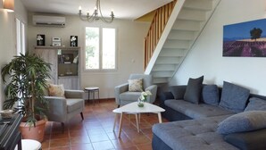 Una sala de estar con una escalera, una araña, un sofá, sillones, una mesa de centro y una planta en maceta.