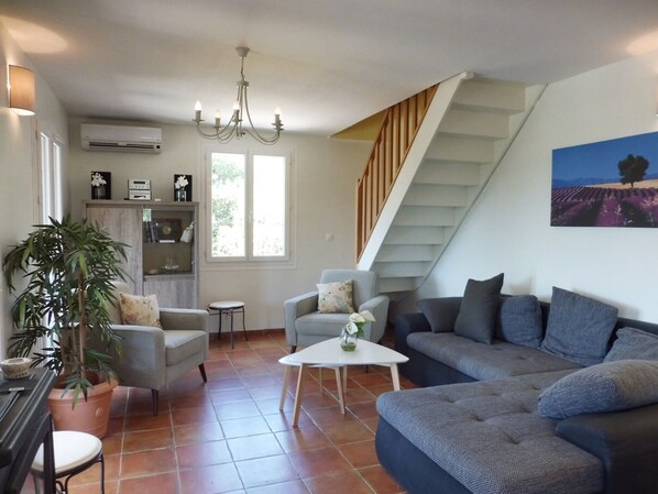 Un salon avec un escalier, un lustre, un canapé, des fauteuils, une table basse et une plante en pot.