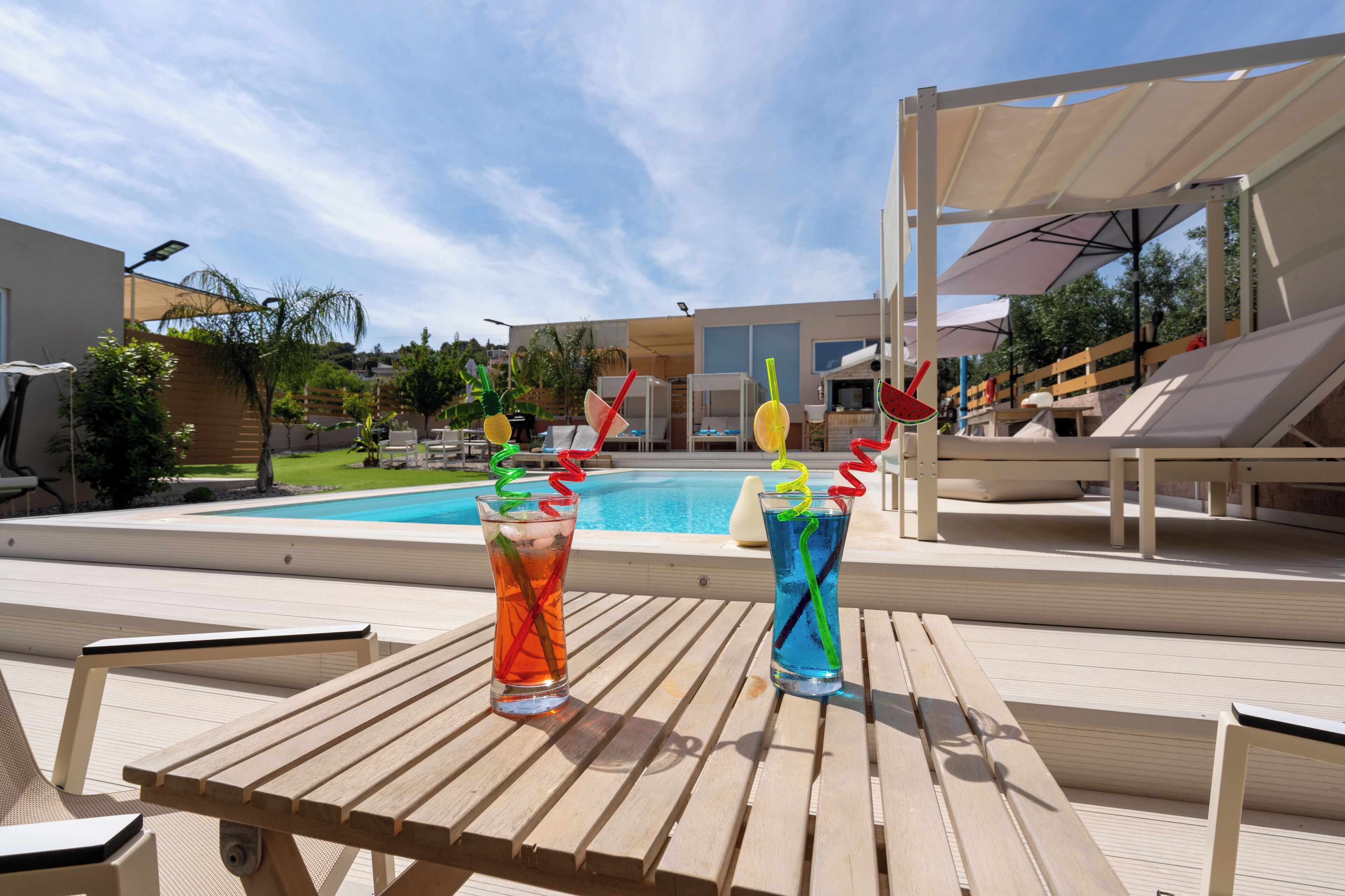 A poolside area with wooden lounge chairs and a table with two drinks.