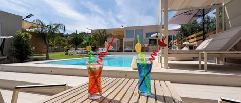 A poolside area with wooden lounge chairs and a table with two drinks.