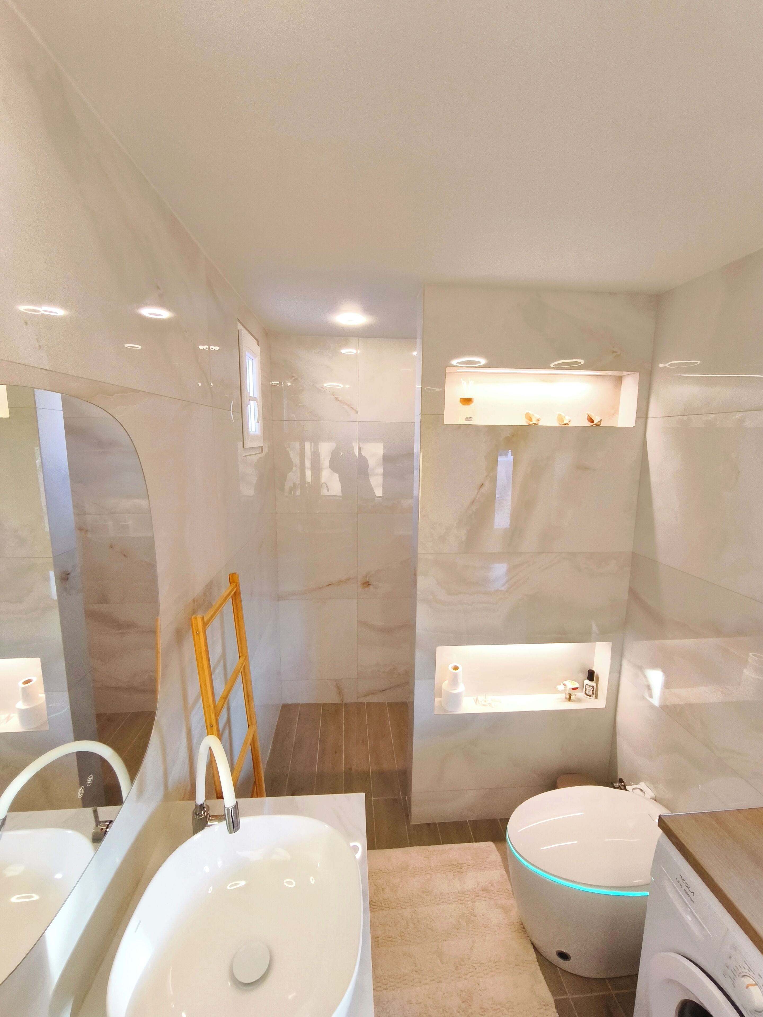 A modern bathroom with a large mirror, a double sink, a toilet, and a built-in washing machine.