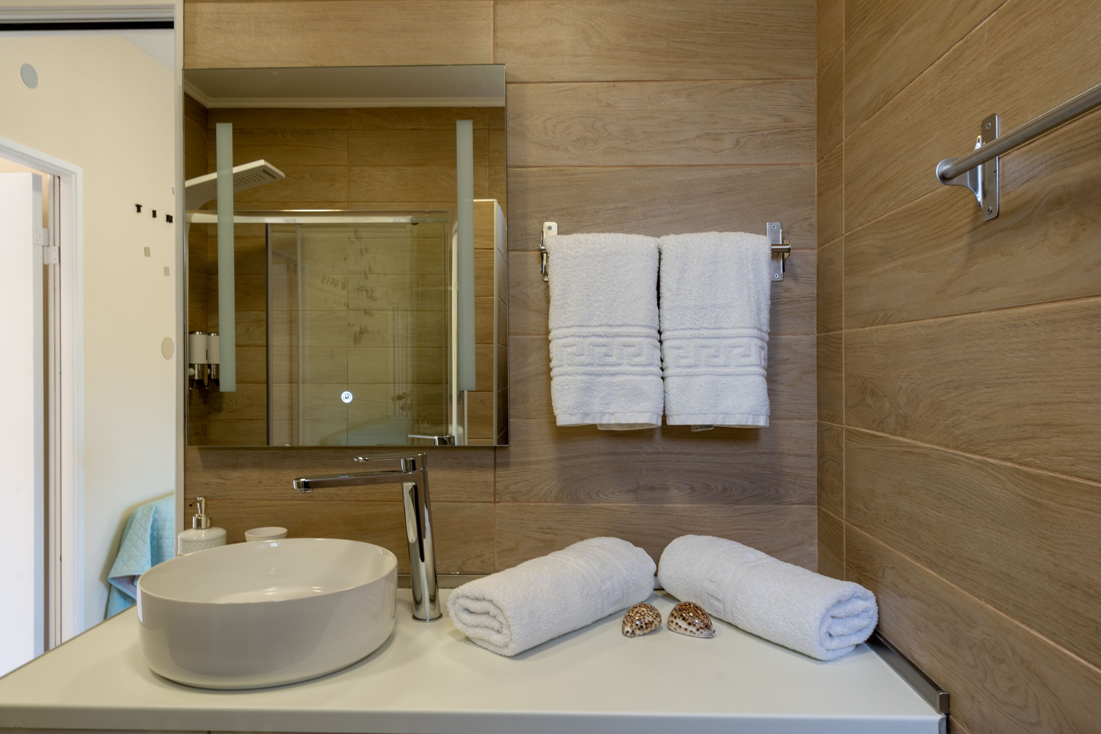 Un baño moderno con un lavamanos grande, un espejo y paredes de madera. Hay dos toallas y un par de pantuflas en el mostrador.