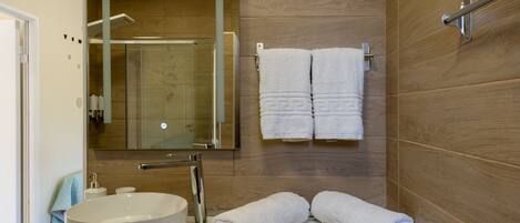 Un baño moderno con un lavamanos grande, un espejo y paredes de madera. Hay dos toallas y un par de pantuflas en el mostrador.