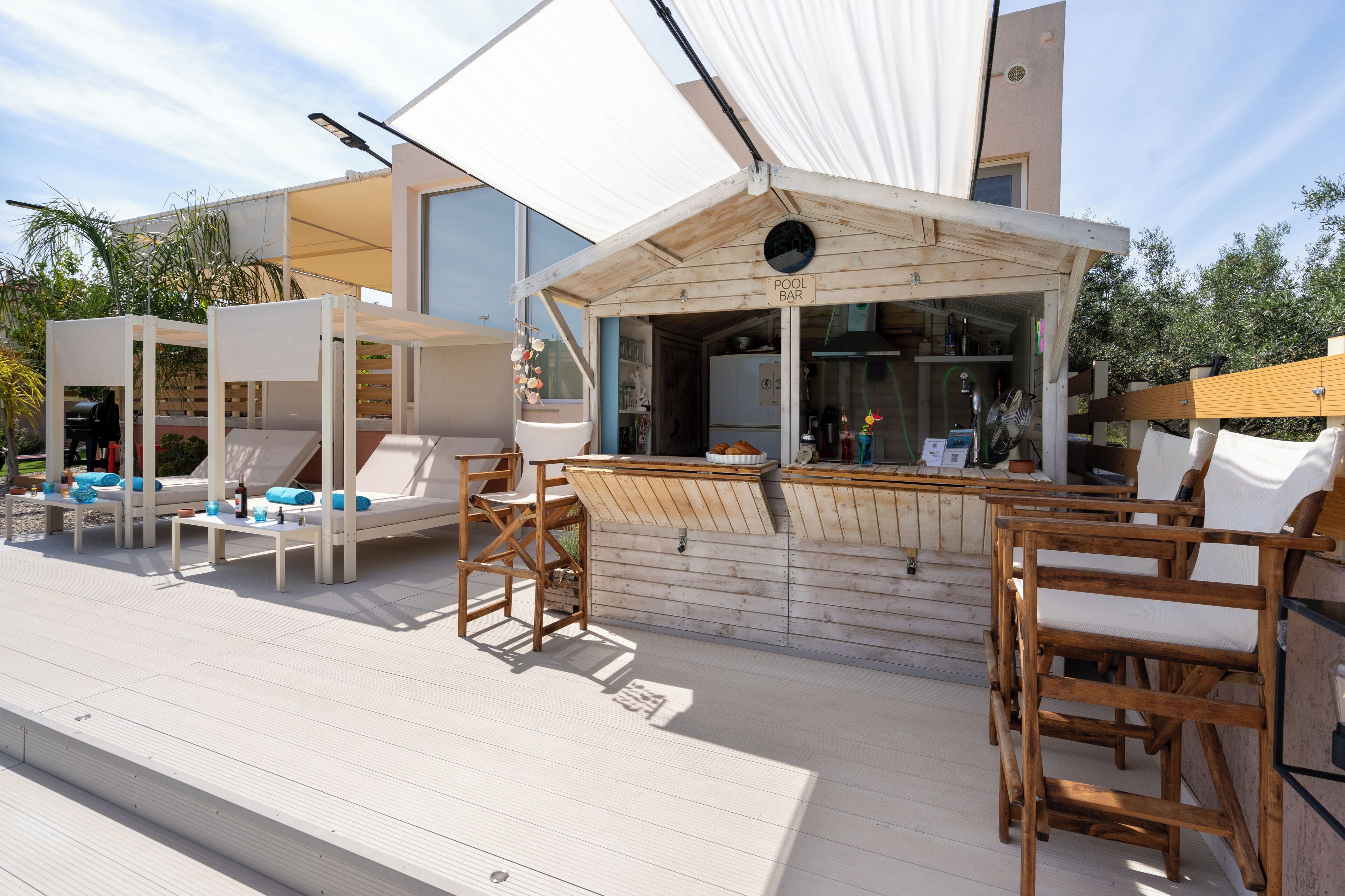 A poolside area with wooden lounge chairs, a bar, and a covered seating area.