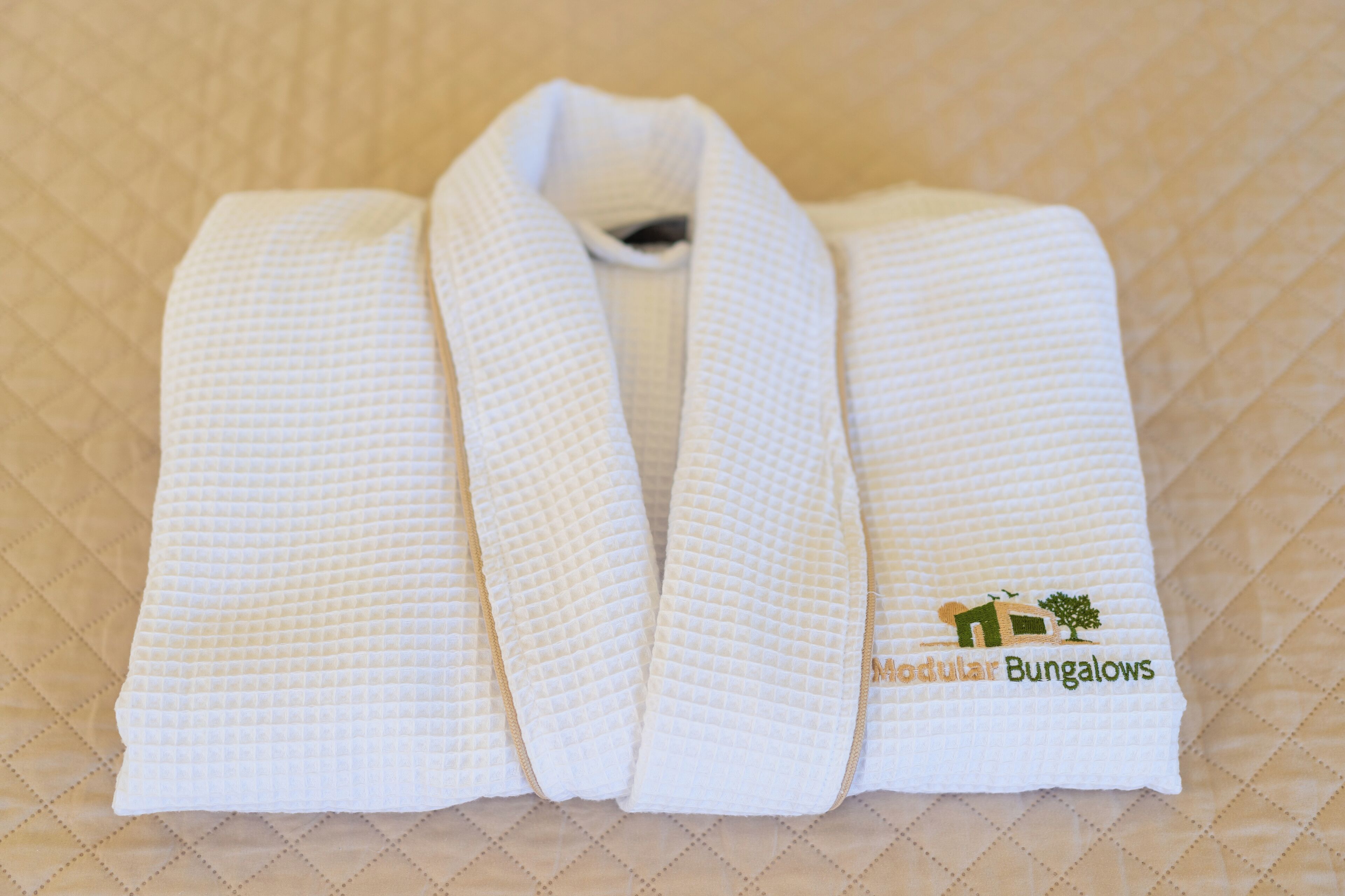 A neatly folded white towel with a logo on it, placed on a quilted surface.