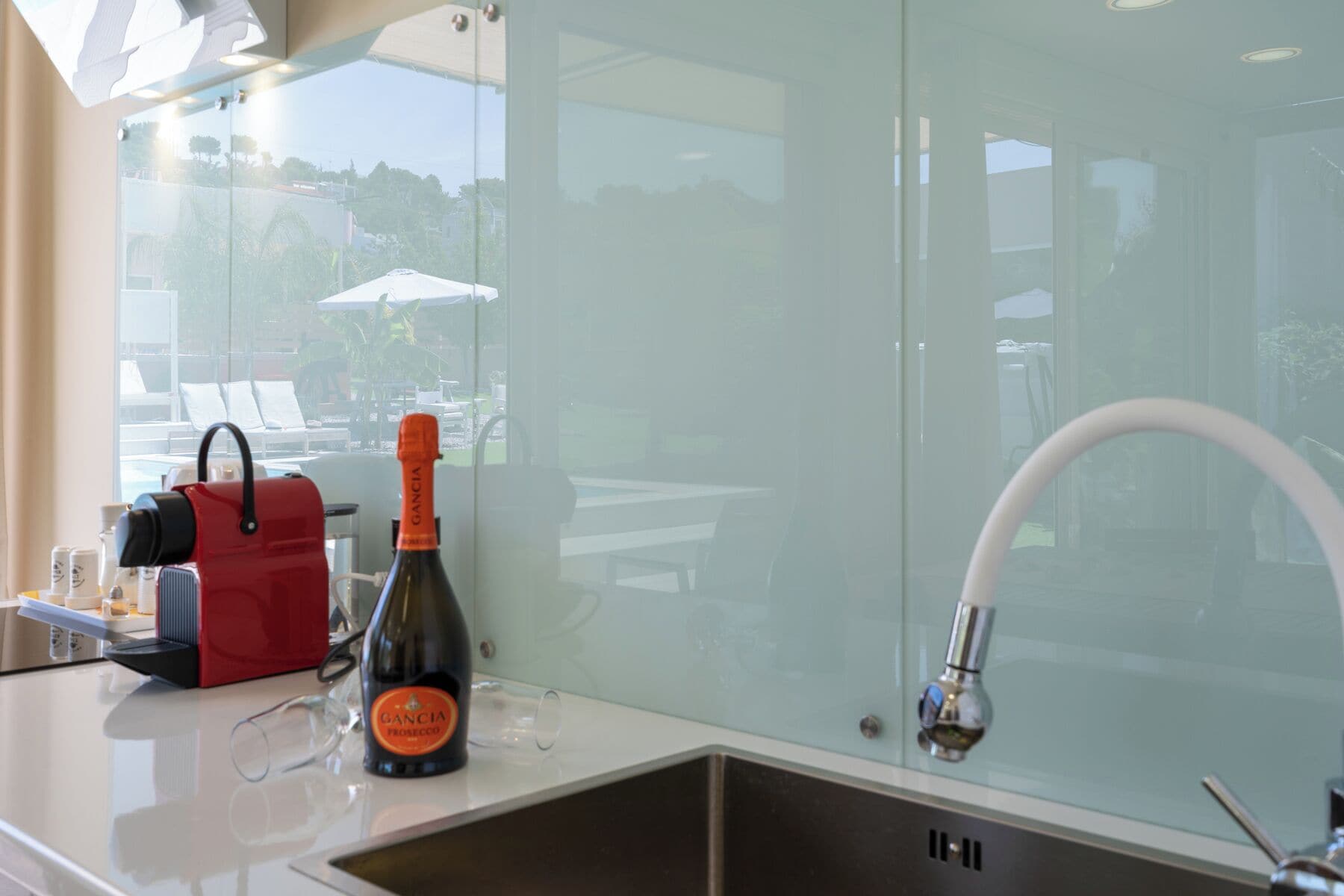 A modern kitchen with a wine bottle, glasses, and a red bag on the counter.