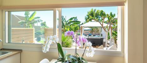 A kitchen with a window view of a garden, a dining table, and a white chair.