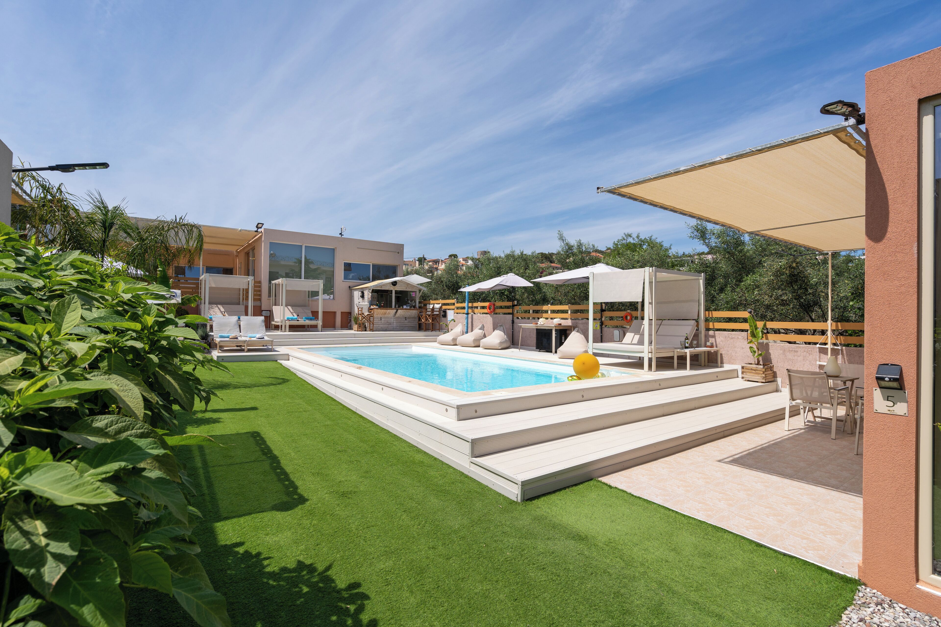 Un espace piscine extérieur moderne, avec un ciel bleu dégagé, une pelouse bien entretenue et un coin salon agrémenté de parasols.