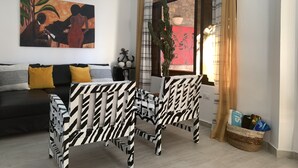 Un salon moderne avec un canapé, deux fauteuils à rayures zébrées, une table et une grande fenêtre avec des rideaux.