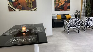 Un salon moderne avec un canapé à motifs noir et blanc, une table basse noire ornée d’assiettes décoratives et deux tableaux accrochés au mur.