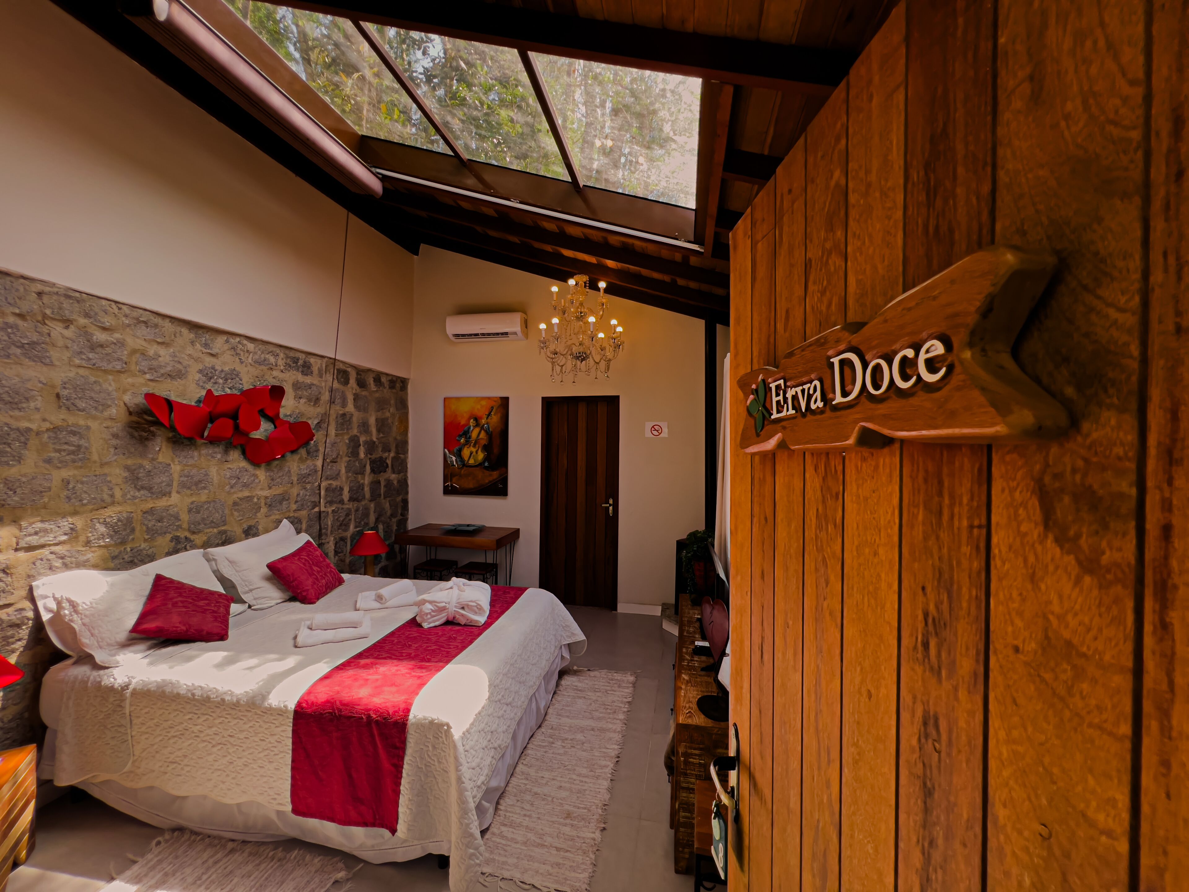 A bedroom with a bed, a wooden wall sign, a stone wall, a chandelier, and a painting.