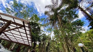 A wooden structure with a metal roof, parked cars, and a small building with a clock. - Espaço Viverde Pousada (Itatiaia)