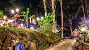 A pathway leading to a building with a rustic design, surrounded by tropical vegetation and illuminated by street lamps. - Espaço Viverde Pousada (Itatiaia)