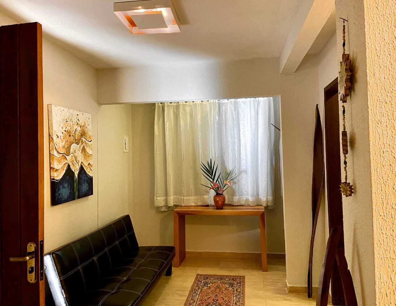 Una sala de estar con un sofá de cuero negro, una mesa de centro de madera, un cuadro en la pared y una ventana con cortinas.