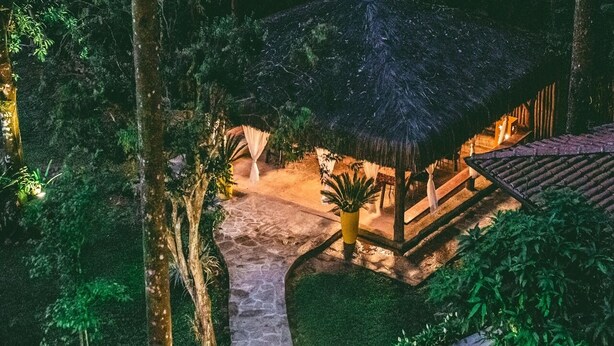 A thatched-roof structure with a stone pathway leading to it, surrounded by lush greenery. - Espaço Viverde Pousada (Itatiaia)