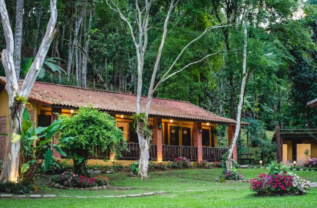 A rustic building with a tiled roof, surrounded by lush greenery and flowering plants.