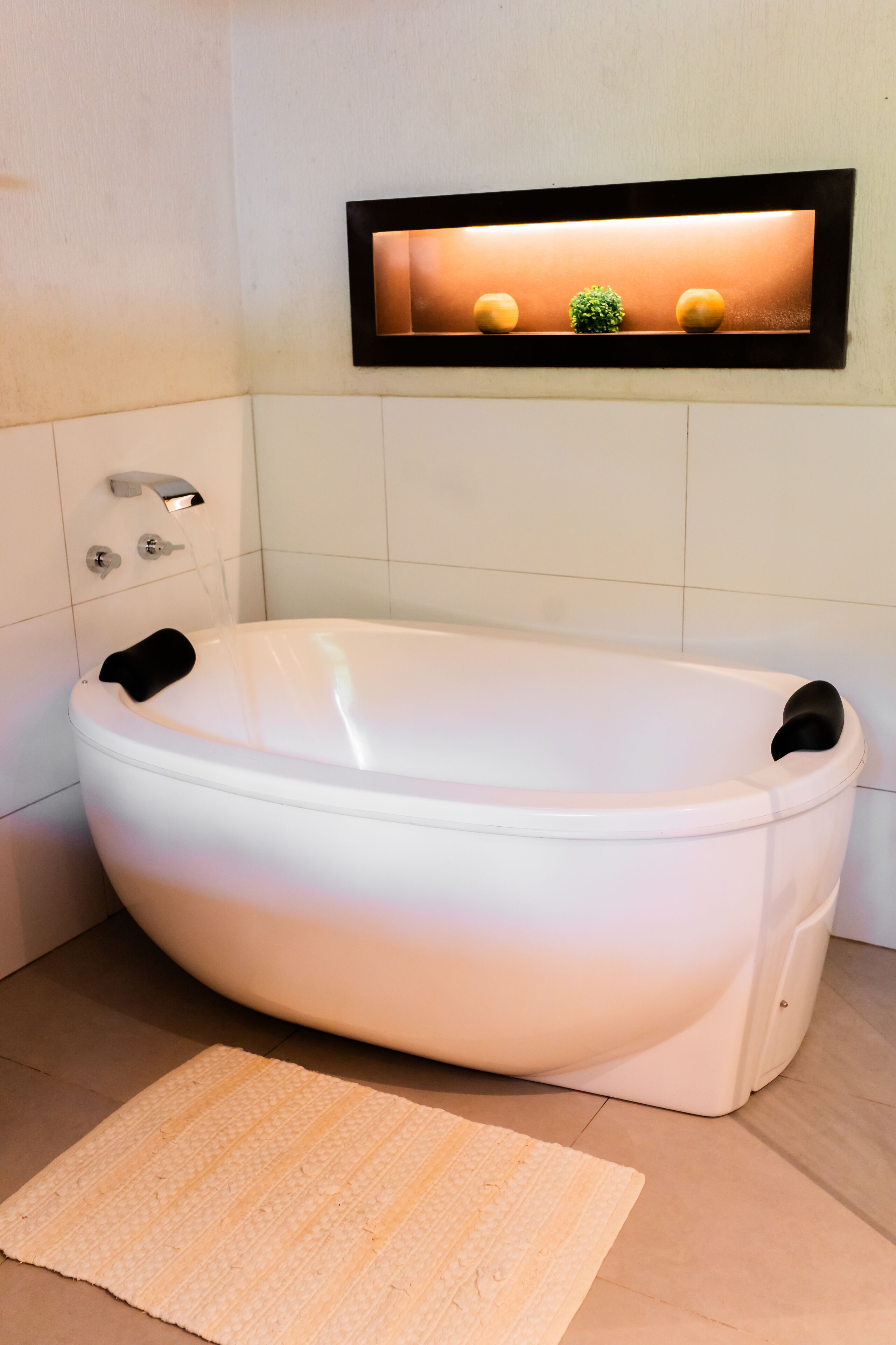 A modern bathroom with a freestanding bathtub, a wall-mounted light fixture, and a small potted plant.
