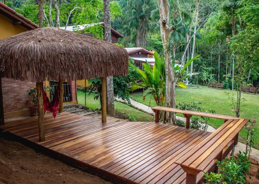A wooden deck with a thatched roof structure, surrounded by lush greenery and a pathway.